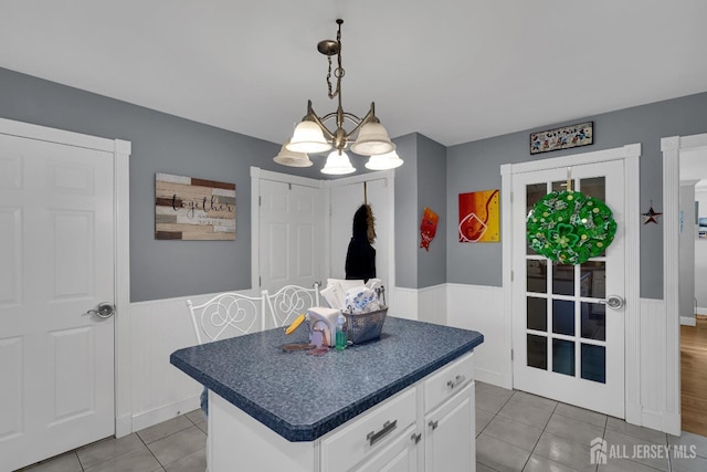 kitchen featuring dark countertops, white cabinets, light tile patterned floors, and a wainscoted wall