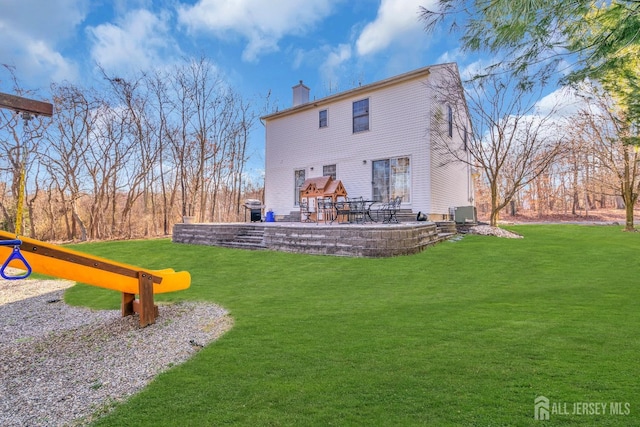 back of house featuring a playground, central AC, a lawn, a chimney, and a patio