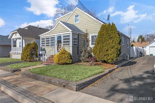 bungalow-style house featuring central AC unit, a detached garage, an outbuilding, roof with shingles, and a front lawn