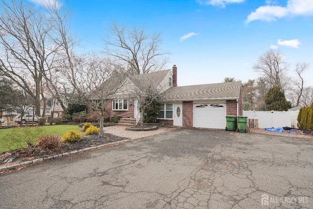 view of front of property with aphalt driveway, an attached garage, brick siding, fence, and a chimney