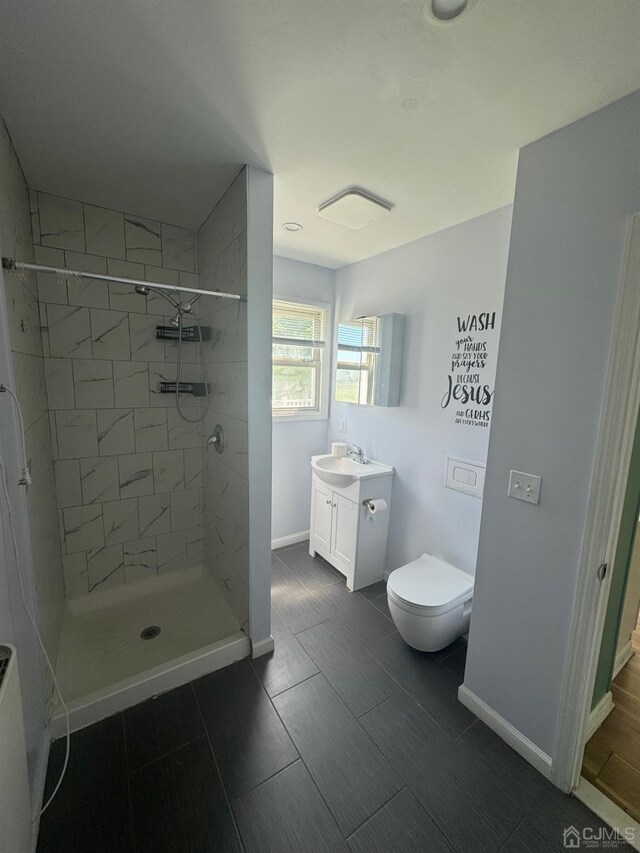 bathroom featuring tile patterned flooring, a tile shower, vanity, and toilet