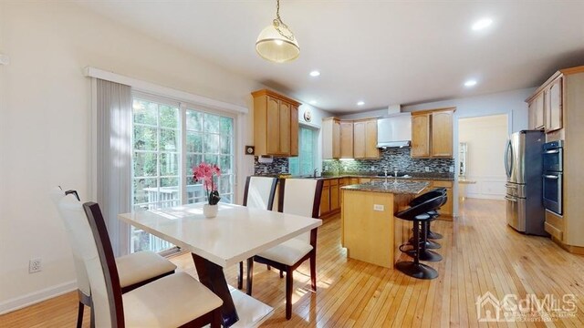 kitchen with a center island, wall chimney exhaust hood, light wood-type flooring, decorative backsplash, and pendant lighting