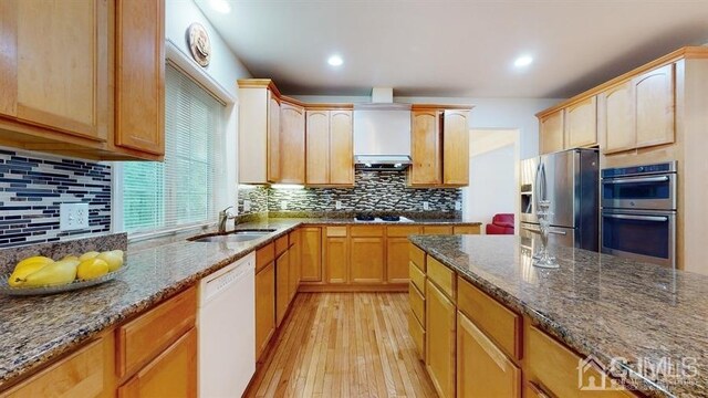 kitchen featuring sink, light wood-type flooring, tasteful backsplash, dark stone counters, and appliances with stainless steel finishes