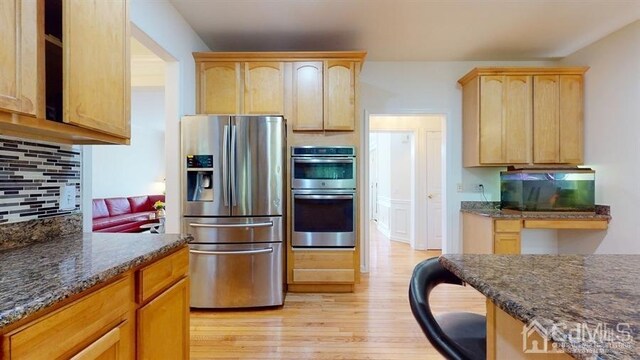 kitchen featuring stainless steel appliances, light hardwood / wood-style flooring, decorative backsplash, light brown cabinetry, and dark stone counters