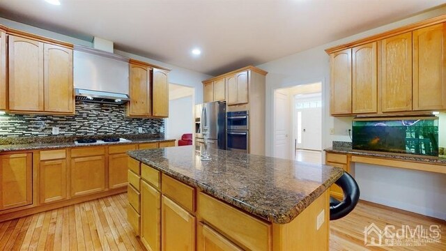 kitchen featuring dark stone countertops, light hardwood / wood-style floors, stainless steel appliances, a center island, and tasteful backsplash