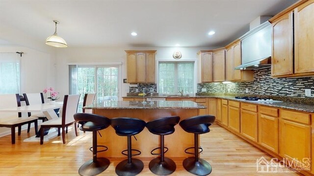 kitchen with white gas stovetop, light wood-type flooring, a center island, dark stone counters, and pendant lighting