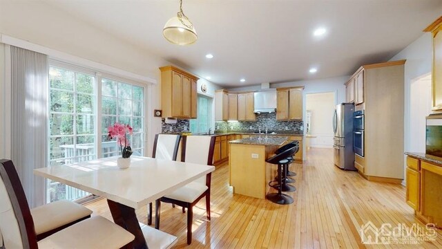 kitchen with decorative light fixtures, a center island, light wood-type flooring, backsplash, and stainless steel fridge