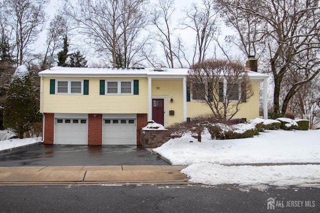 bi-level home with aphalt driveway, a chimney, brick siding, and a garage