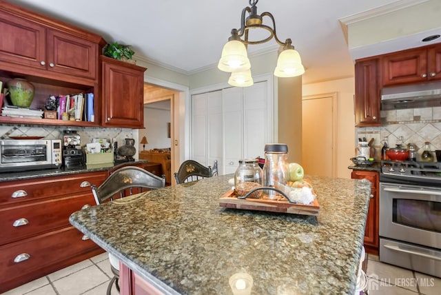 kitchen featuring light tile patterned floors, stainless steel gas range oven, a center island with sink, decorative backsplash, and dark stone counters