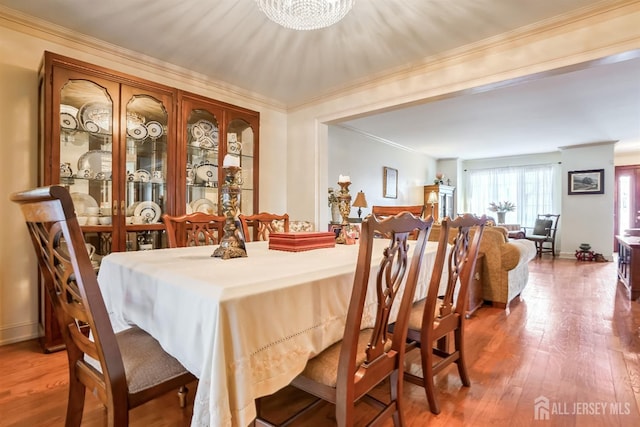 dining area with a notable chandelier, wood-type flooring, and ornamental molding