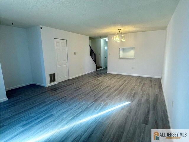 empty room featuring an inviting chandelier, a textured ceiling, and dark wood-type flooring