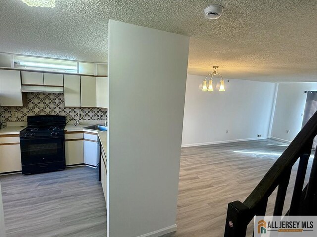 kitchen with pendant lighting, light hardwood / wood-style floors, backsplash, black range with gas cooktop, and sink