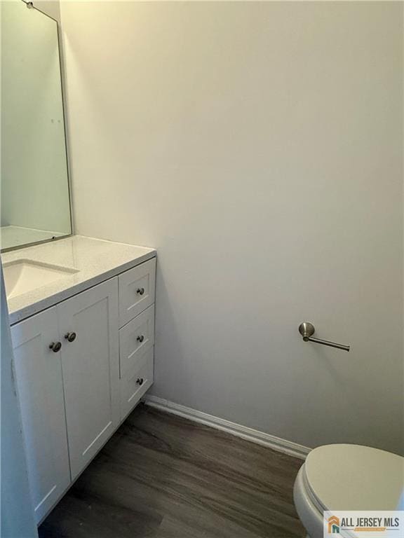 bathroom with vanity, toilet, wood finished floors, and baseboards