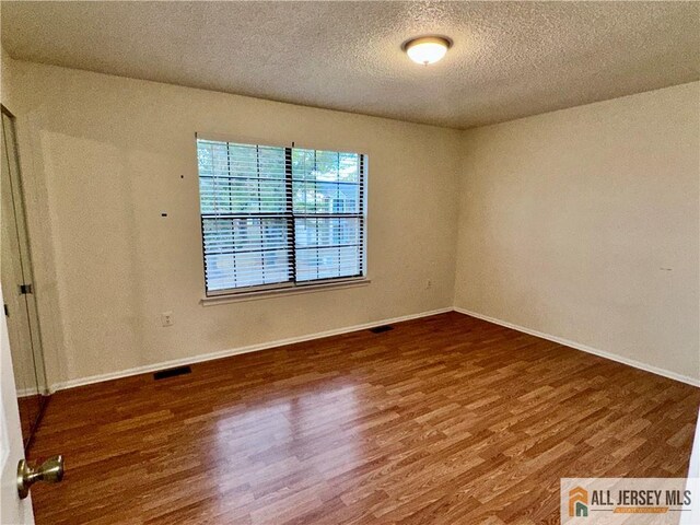 empty room featuring visible vents, baseboards, a textured ceiling, and wood finished floors