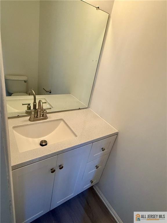 half bathroom with toilet, wood finished floors, and vanity