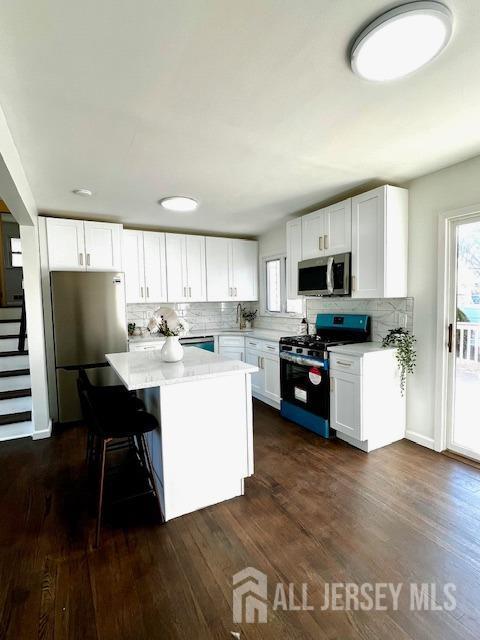 kitchen with dark wood-type flooring, appliances with stainless steel finishes, white cabinetry, and a center island