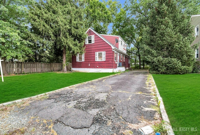 view of home's exterior featuring driveway, a lawn, and fence