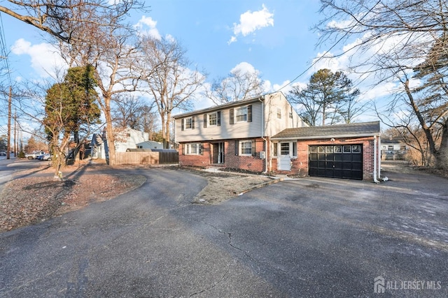 colonial-style house featuring a garage, fence, aphalt driveway, and brick siding