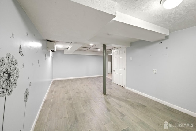 finished below grade area featuring baseboards, a wall mounted AC, a textured ceiling, and light wood-style floors