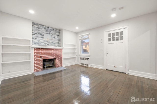 unfurnished living room with dark wood-style floors, built in shelves, radiator heating unit, and baseboards