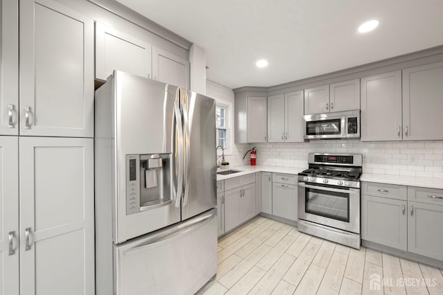 kitchen with tasteful backsplash, appliances with stainless steel finishes, gray cabinets, light countertops, and a sink