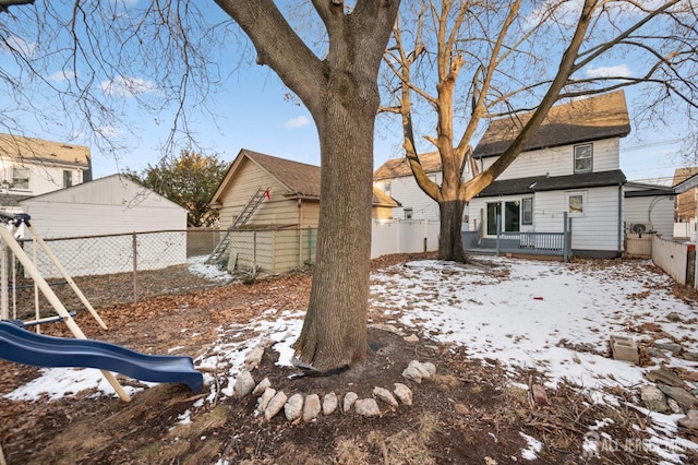 snowy yard featuring a garage, a fenced backyard, and a playground