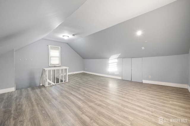 additional living space featuring vaulted ceiling, light wood-style flooring, and baseboards