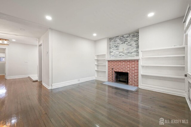 unfurnished living room with a brick fireplace, dark hardwood / wood-style floors, and built in features