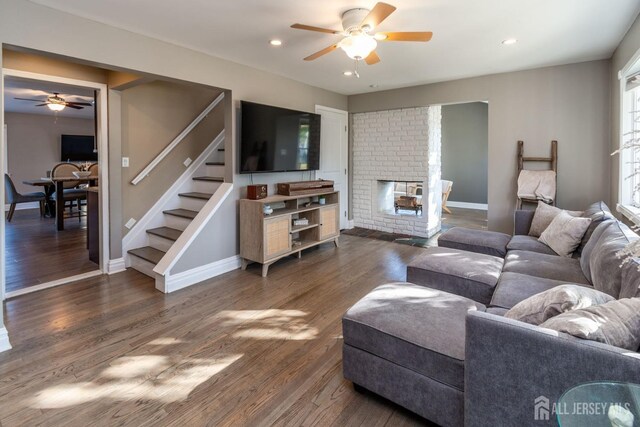 living room featuring ceiling fan, a fireplace, and dark wood-type flooring