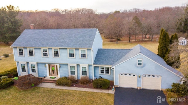 view of front of home featuring a front yard, an attached garage, driveway, and a forest view