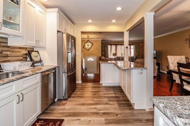 kitchen featuring white cabinetry, stainless steel appliances, decorative columns, light stone counters, and light hardwood / wood-style floors