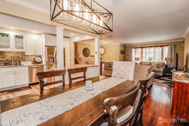 dining space with dark wood-type flooring, ornamental molding, sink, and a notable chandelier