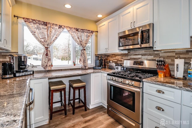 kitchen featuring appliances with stainless steel finishes, light stone counters, tasteful backsplash, white cabinets, and light wood-type flooring