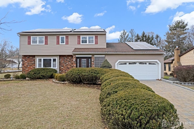 view of front of property with a garage, decorative driveway, roof mounted solar panels, a front lawn, and brick siding