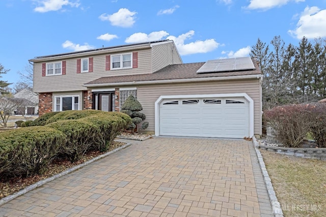 view of front facade featuring an attached garage, solar panels, decorative driveway, and brick siding