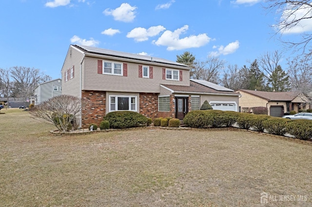 colonial house featuring brick siding, a front lawn, an attached garage, and roof mounted solar panels