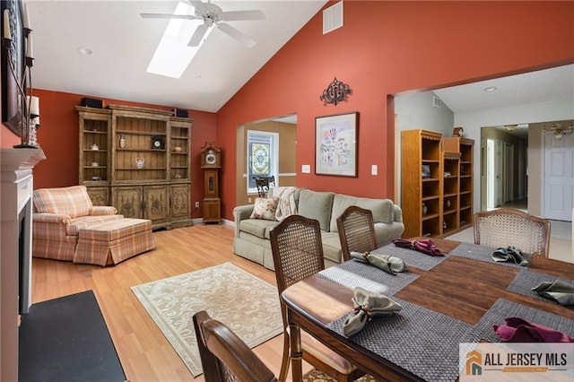 living room with light wood-type flooring, visible vents, a skylight, a fireplace, and ceiling fan