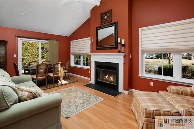 living room with plenty of natural light, light wood-style floors, baseboards, and a fireplace with flush hearth