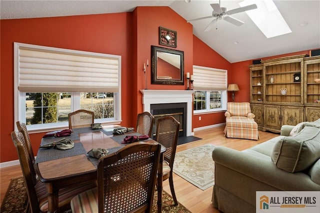 living area featuring vaulted ceiling with skylight, a healthy amount of sunlight, light wood-style flooring, and a fireplace with flush hearth