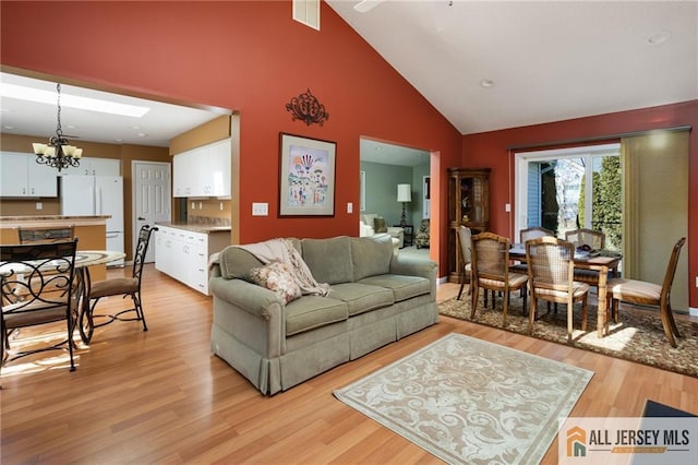 living area with a chandelier, visible vents, light wood-style flooring, and high vaulted ceiling