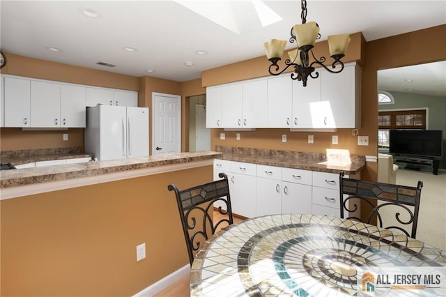 kitchen featuring recessed lighting, freestanding refrigerator, white cabinets, lofted ceiling with skylight, and a notable chandelier