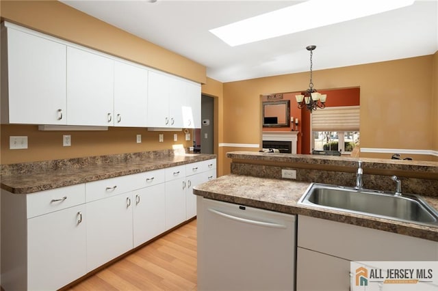 kitchen with dishwasher, light wood-style floors, hanging light fixtures, white cabinetry, and a sink