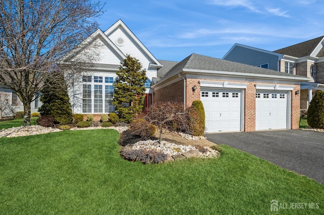 view of front of home with driveway, a shingled roof, an attached garage, a front lawn, and brick siding