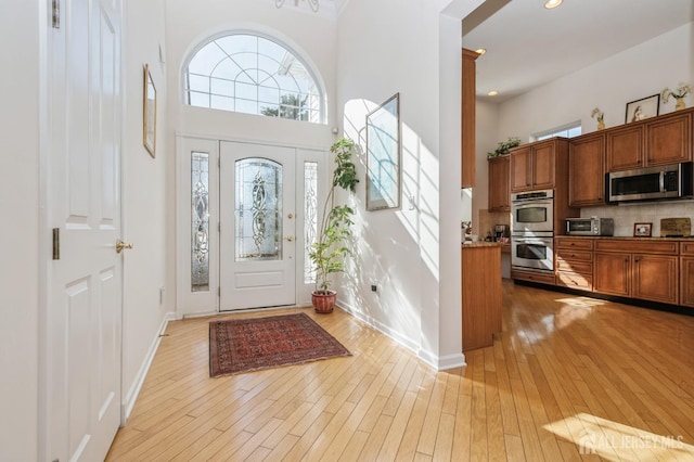 foyer entrance with a high ceiling, recessed lighting, light wood-style flooring, and baseboards