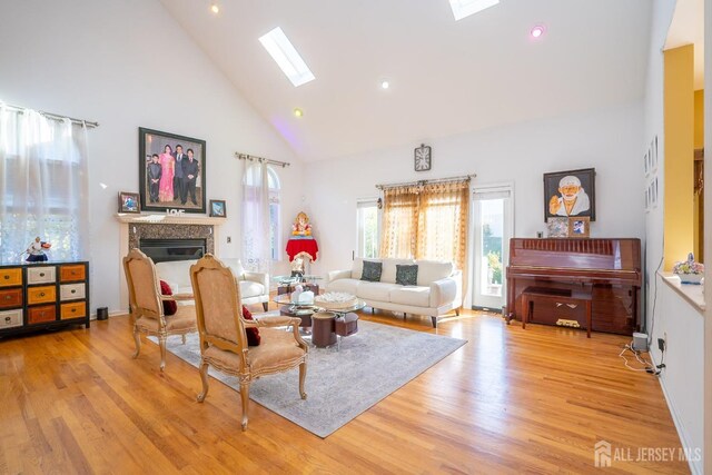 living room featuring a skylight, high vaulted ceiling, and light hardwood / wood-style floors