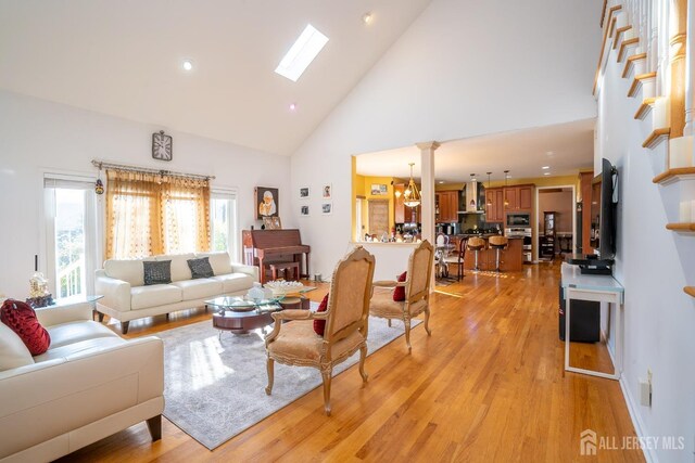 living room with a skylight, an inviting chandelier, high vaulted ceiling, and light hardwood / wood-style flooring