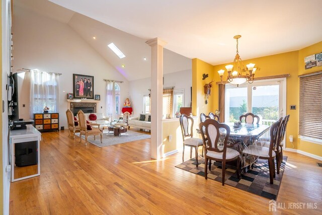 dining area with an inviting chandelier, high vaulted ceiling, light hardwood / wood-style floors, and ornate columns