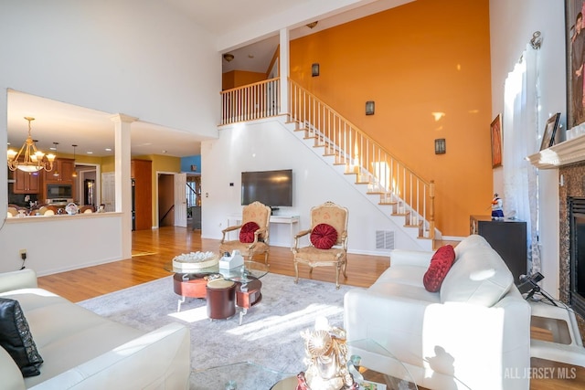 living room featuring an inviting chandelier, a towering ceiling, light hardwood / wood-style floors, and decorative columns