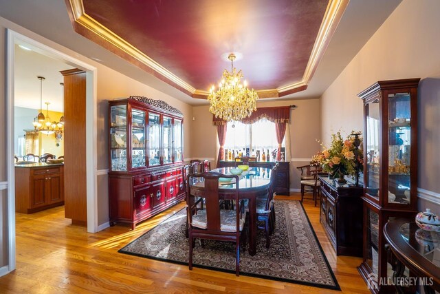 dining area featuring crown molding, light wood-type flooring, an inviting chandelier, and a tray ceiling