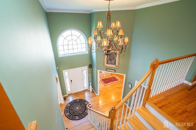 foyer entrance featuring hardwood / wood-style floors, a notable chandelier, ornamental molding, and a high ceiling